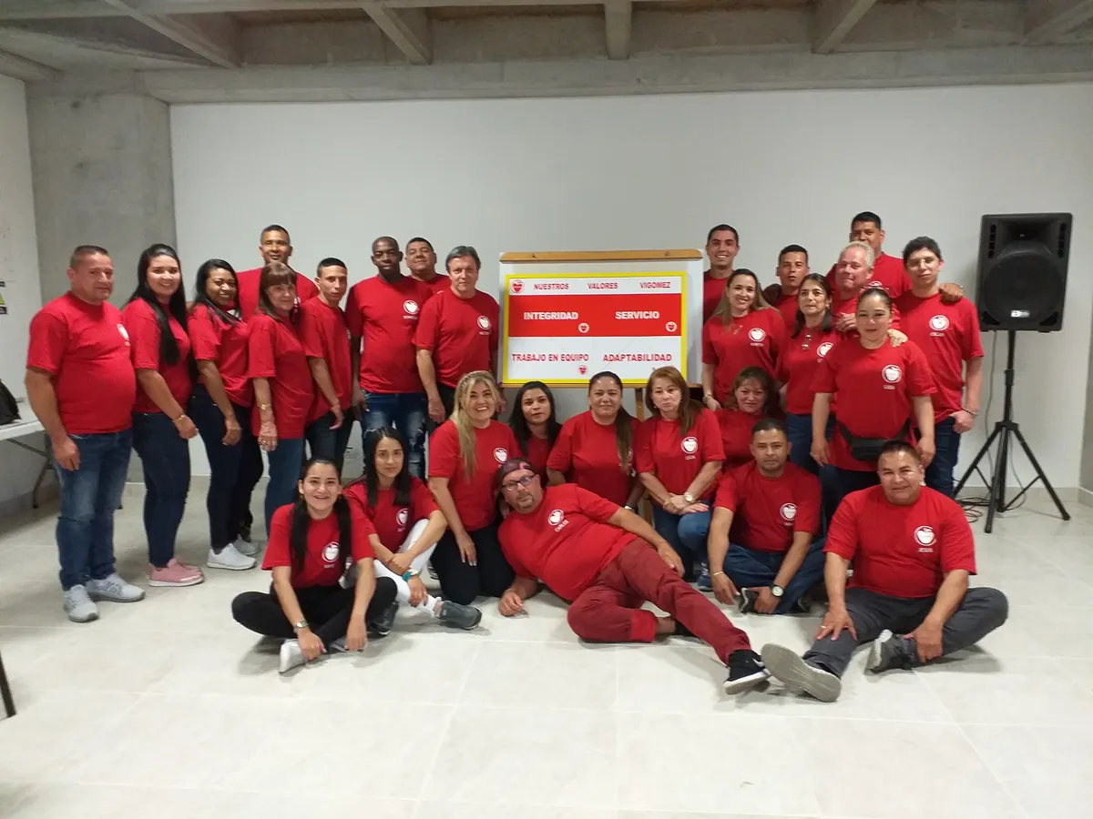 El equipo de Vigomez, en camiseta roja de la empresa, reunido junto al tablero de sus cuatro valores: integridad, servicio, trabajo en equipo y adaptabilidad